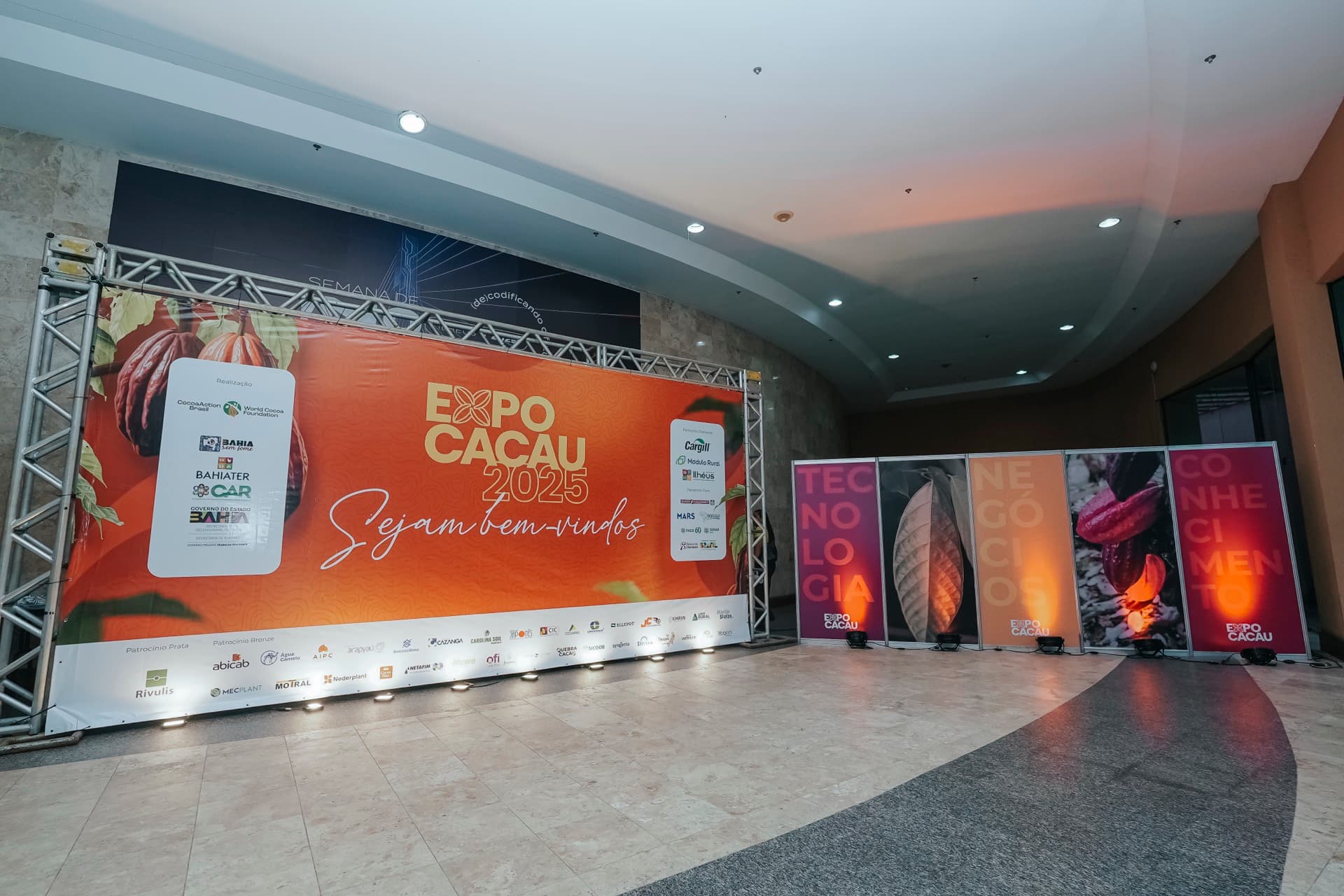 Entrada da Expo Cacau 2025 com banner de boas-vindas e parede de patrocinadores