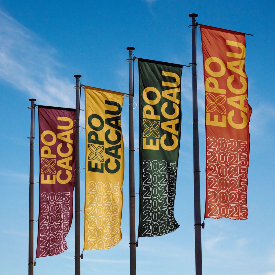 Bandeiras da ExpoCacau em verde, amarelo e vermelho, hasteadas contra o céu