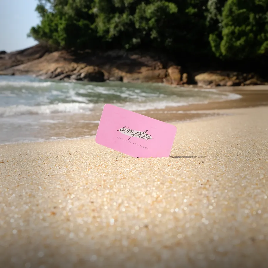 Cartão de visita rosa da Simples fincado na areia de uma praia.