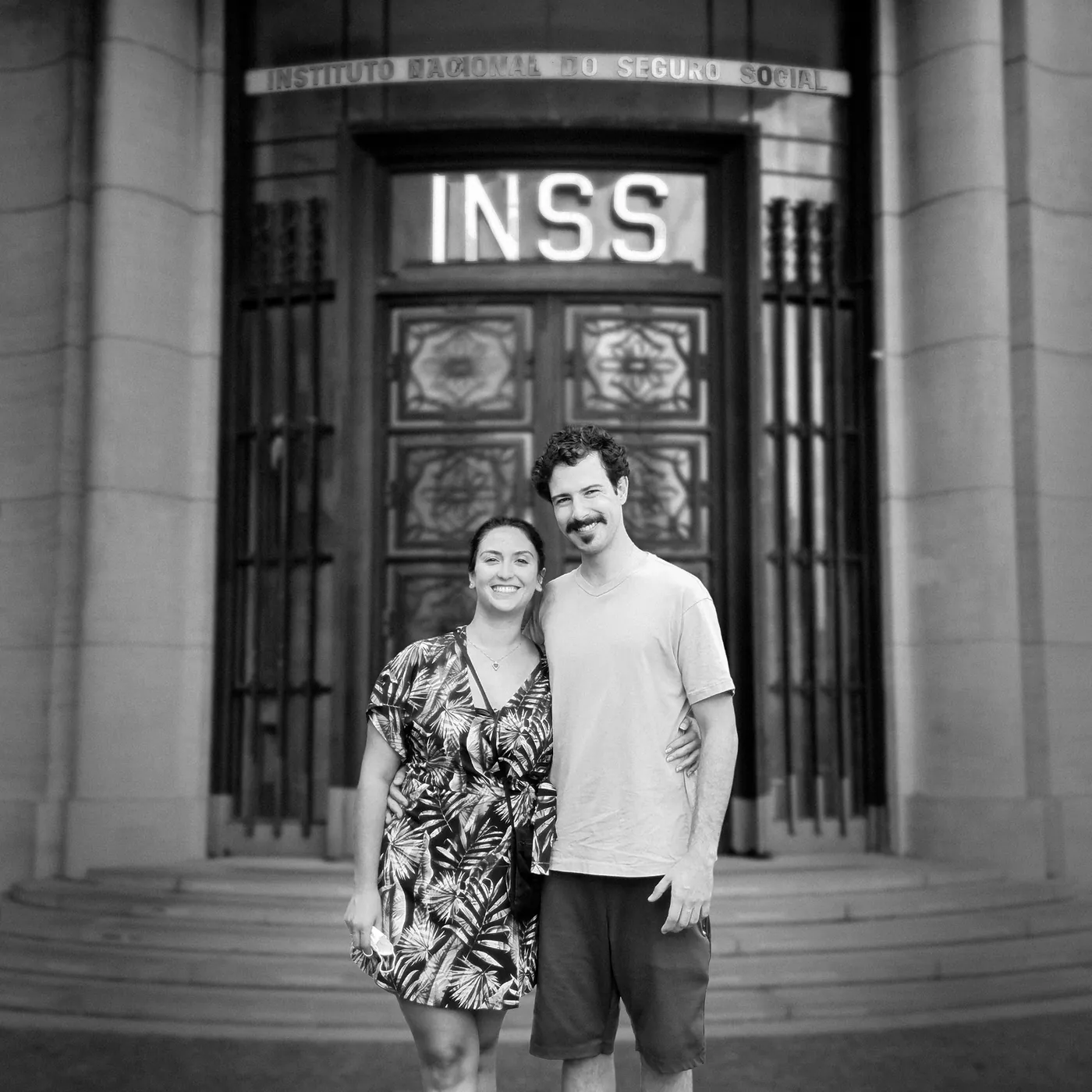 Gabriel e Lívia, os dois sócios da Simples, lado a lado na porta do prédio do INSS, em preto e branco.